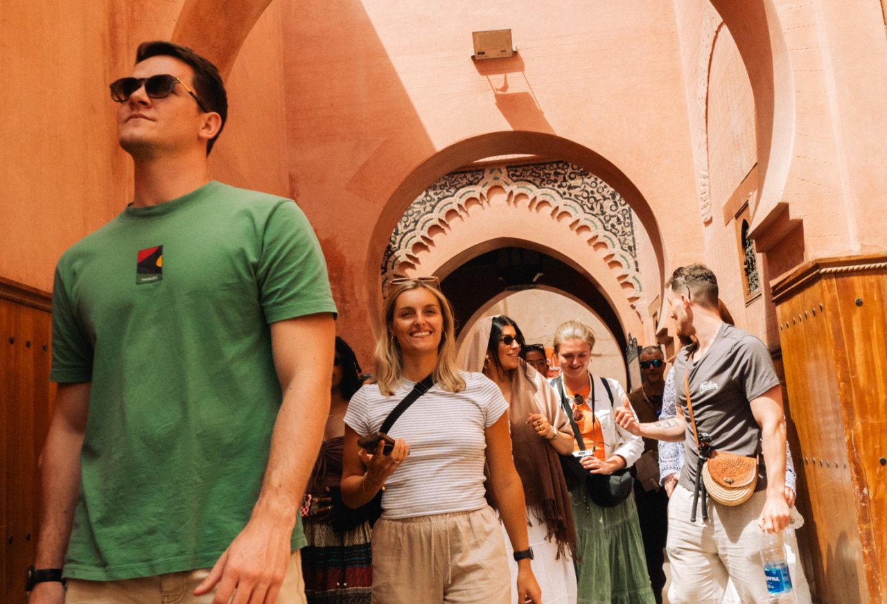 A group of travellers smile and explore Marrakech, Morocco, surrounded by terracotta-colored walls and intricate archways.