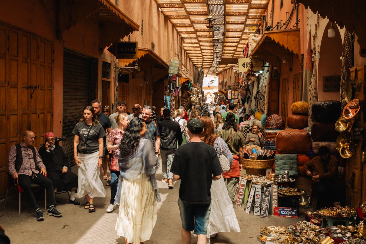 A group of young travellers on a group tour explore the markets in Morocco with a local guide who discusses the history and facts about the city
