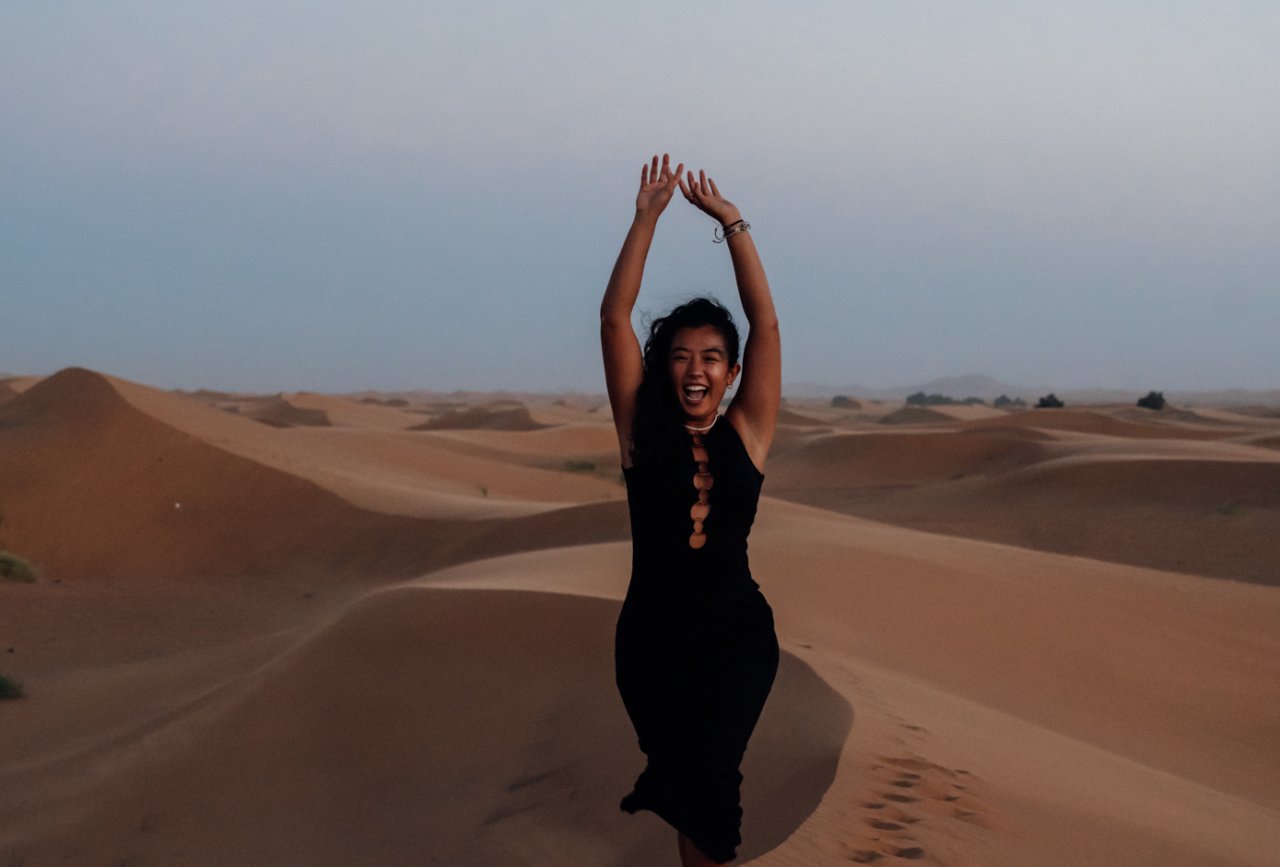 Young female solo traveller poses with the backdrop of the Sahara desert in Morocco
